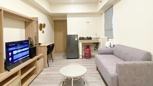 A compact living space with a kitchenette, a dining area, a sofa, and a TV on a wooden shelf. - Good Deal And Comfortable 2Br Meikarta Apartment (Cikarang)