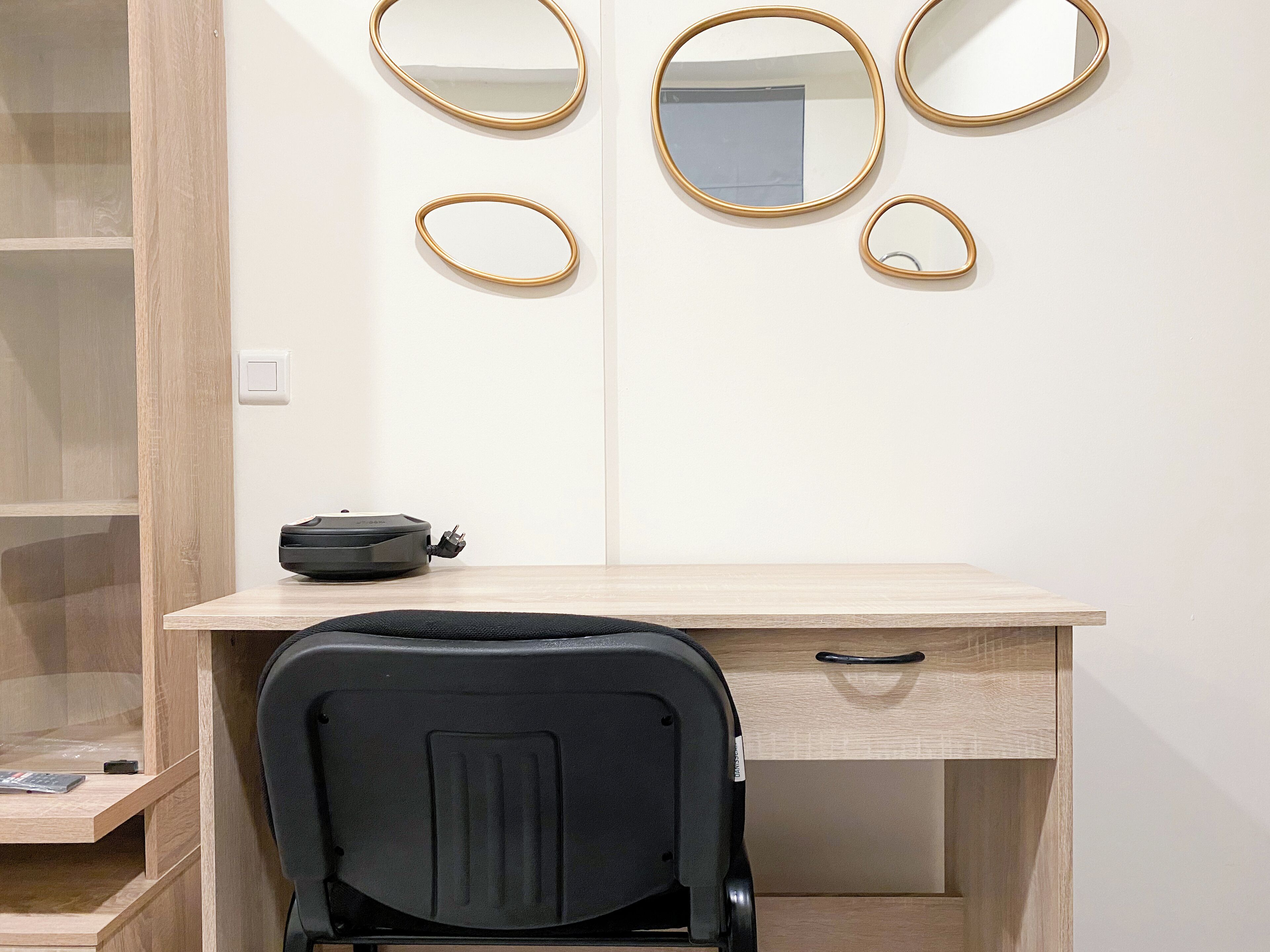 A room with a wooden desk, a black chair, and three mirrors on the wall.