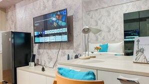 Una habitación de hotel moderna con un televisor de pantalla plana montado en la pared, una cama con almohada azul, una mesita de noche y una silla de madera.