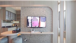 A modern hotel room with a flat-screen TV mounted on a textured wall, a small desk with a laptop, and a seating area with a cushioned bench. - Beautiful And Modern Studio At Benson Supermall Mansion Apartment (Surabaya)