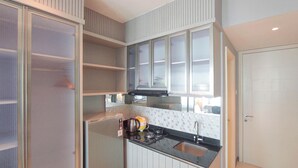 A modern kitchen with a gas stove, a kettle, and a microwave. There is a window above the stove and a door on the right. - Beautiful And Modern Studio At Benson Supermall Mansion Apartment (Surabaya)