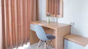 Une chambre moderne avec un bureau en bois, une chaise bleue, un vase de fleurs et un miroir au mur.