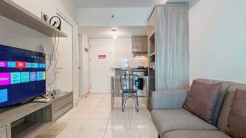A modern living room with a flat-screen TV, a sofa, and a dining area with a chair and table.