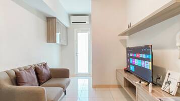 A modern living room with a beige sofa, a flat-screen TV on a wooden stand, and a door leading to another room.