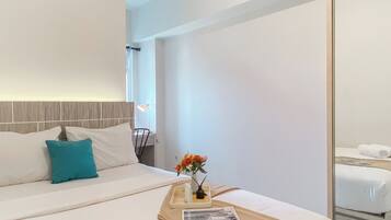 A modern hotel room with a neatly made bed, a bedside table with a vase of flowers, and a window with a view of the outside.