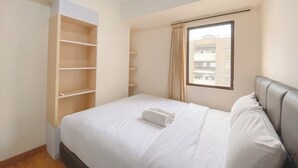 Un dormitorio ordenado con una cama, un armario empotrado y una ventana con vistas a edificios.