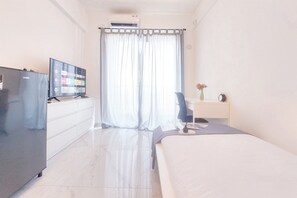 Una camera d'albergo con un letto, una scrivania, una sedia, una TV e un frigorifero.
