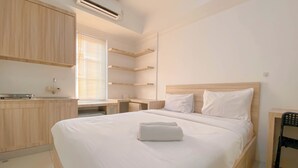 A modern hotel room with a wooden bed, white linens, a small desk, and built-in shelves. - Simply Look And Homey Studio Paltrow City Apartment (Semarang)