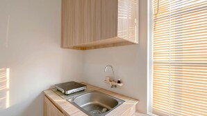 A compact kitchen with a sink, a small countertop, and a window with blinds. - Simply Look And Homey Studio Paltrow City Apartment (Semarang)
