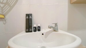 A white bathroom sink with a silver faucet, two toothbrushes, and two tubes of toothpaste. - Simply Look And Homey Studio Paltrow City Apartment (Semarang)