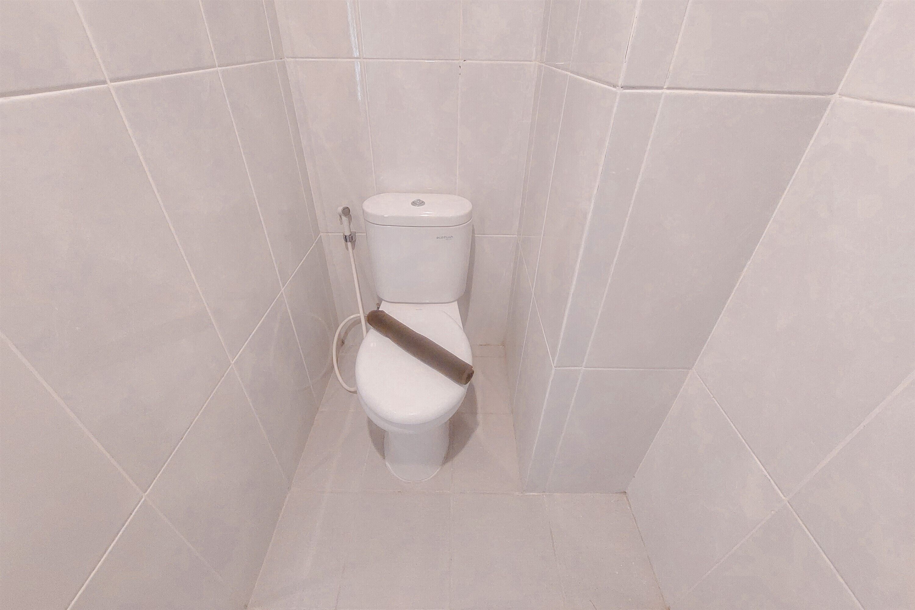 A small, white, wall-mounted toilet in a tiled bathroom with a single flush handle.