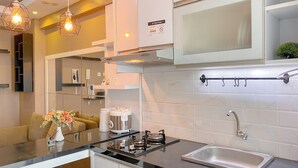 Cocina moderna con encimera negra, pileta de acero inoxidable y horno integrado. Hay un armario blanco sobre la pileta y una planta pequeña en la encimera.