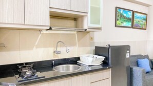 A compact kitchen with a sink, a stove, and a refrigerator. There is a window above the sink and a wall-mounted shelf. - Spacious And Homey 3Br At Green Bay Pluit Apartment (Jakarta)