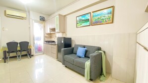 A compact living space with a kitchenette, a sofa with a blanket, and two chairs. - Spacious And Homey 3Br At Green Bay Pluit Apartment (Jakarta)