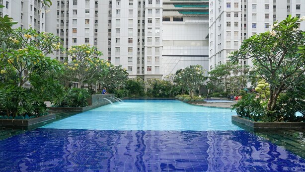 A swimming pool surrounded by greenery and tall residential buildings. - Spacious And Homey 3Br At Green Bay Pluit Apartment (Jakarta)