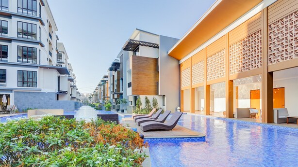 A modern hotel with a swimming pool, lounge chairs, and a well-maintained garden area. - Good Place And Homey 3Br At Asatti Apartment (Pagedangan)