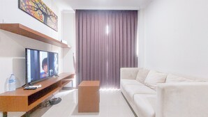 A modern living room with a flat-screen TV on a wooden console, a white sofa, and a large window with curtains. - Good Place And Homey 3Br At Asatti Apartment (Pagedangan)