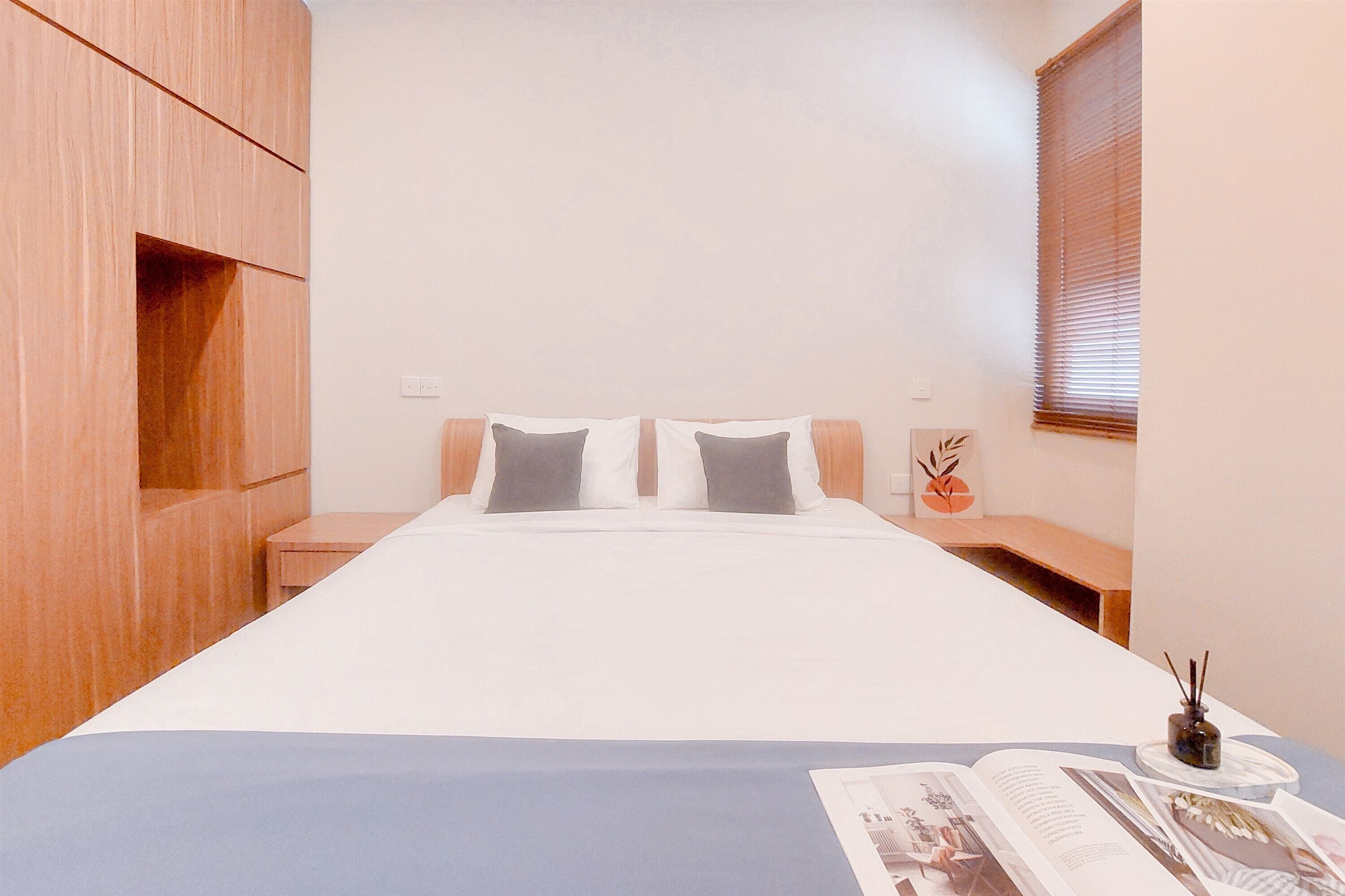 A bedroom with a bed, two bedside tables, a nightstand, a window with blinds, and a small decorative item on the nightstand.
