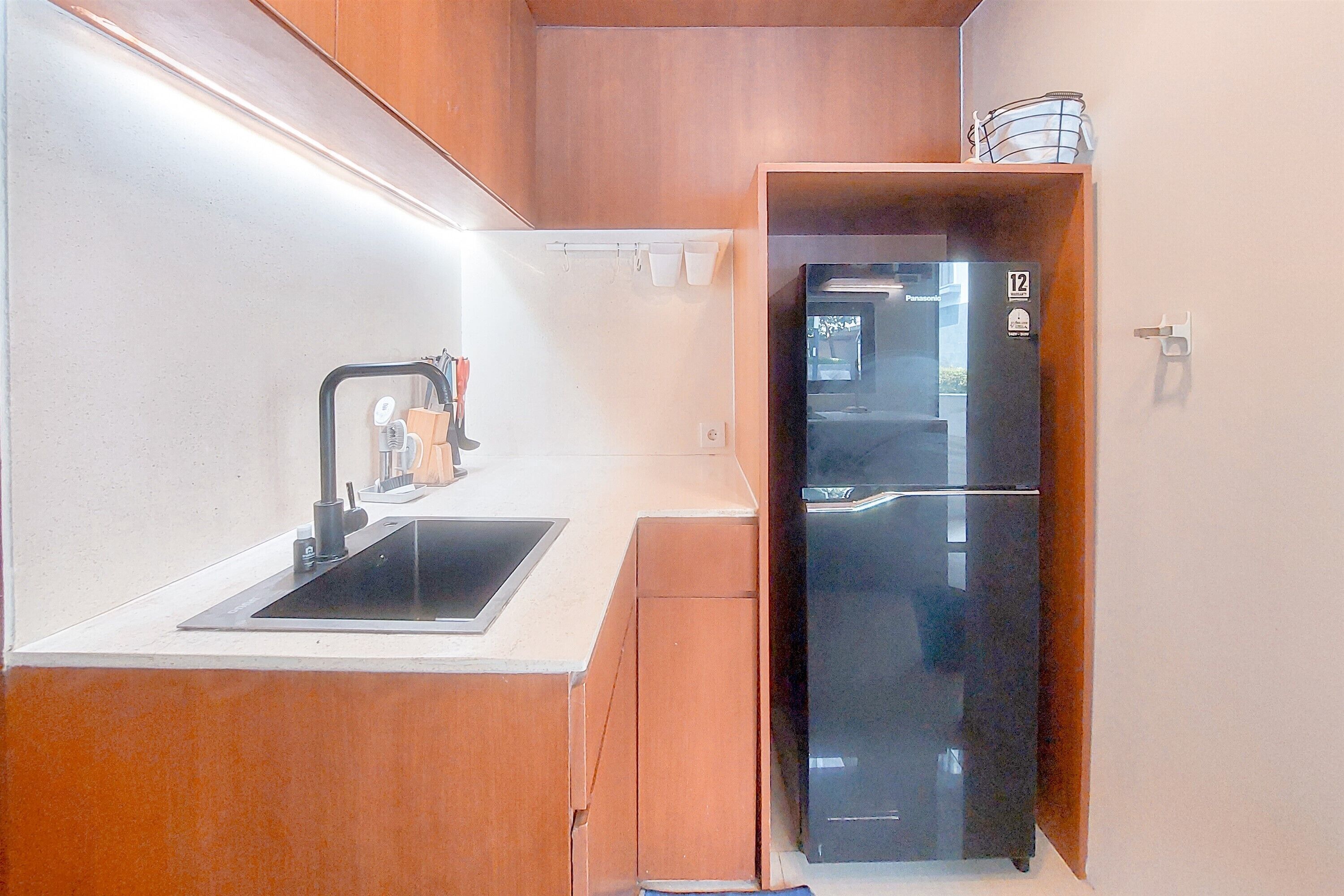 A compact kitchen with a black refrigerator, a sink, and wooden cabinets.