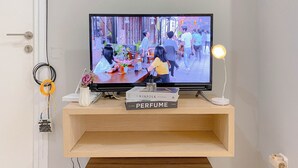 A television mounted on a wooden shelf displaying a scene with people walking outdoors. - Best Choice And Modern 2Br Green Pramuka City Apartment (Jakarta)