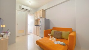 A compact living space with a kitchenette, a sofa, and a small table with a vase and a cup. - Best Choice And Modern 2Br Green Pramuka City Apartment (Jakarta)