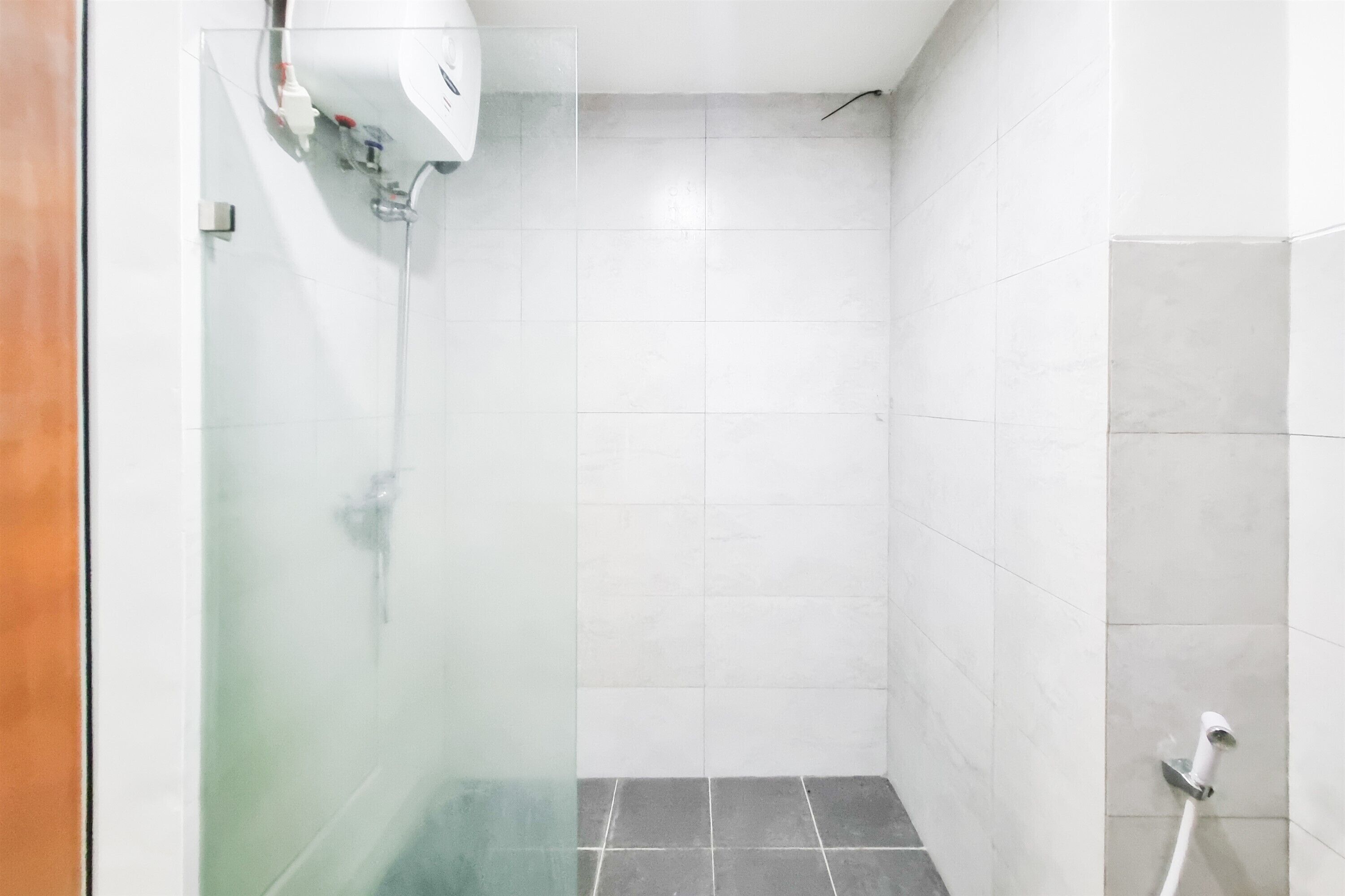 A bathroom with white tiles, a glass shower enclosure, and a white towel dispenser.