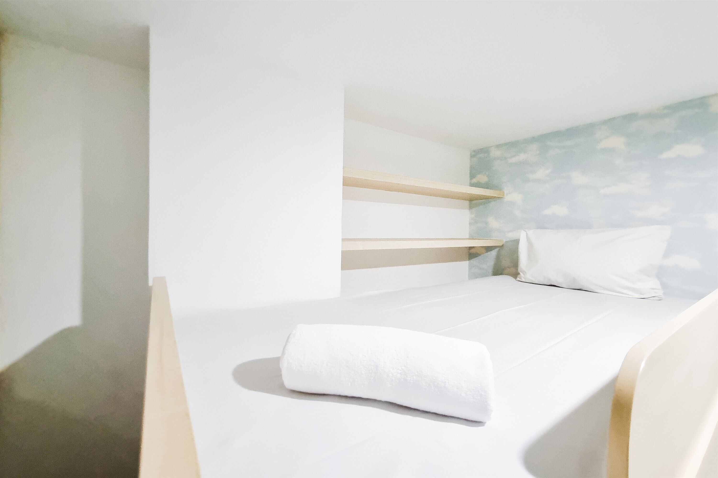 A bunk bed with a white mattress and pillow, a wooden headboard, and a wall with a cloud pattern.