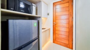 A compact kitchen with a refrigerator, microwave, and a wooden door. - Good Place And Homey 2Br At Green Park Yogyakarta Apartment (Depok)