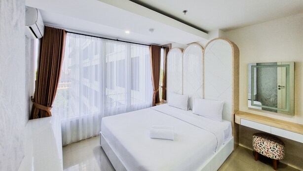 A modern hotel room with a large bed, a bedside table, a mirror, and a window with curtains. - Good Place And Homey 2Br At Green Park Yogyakarta Apartment (Depok)