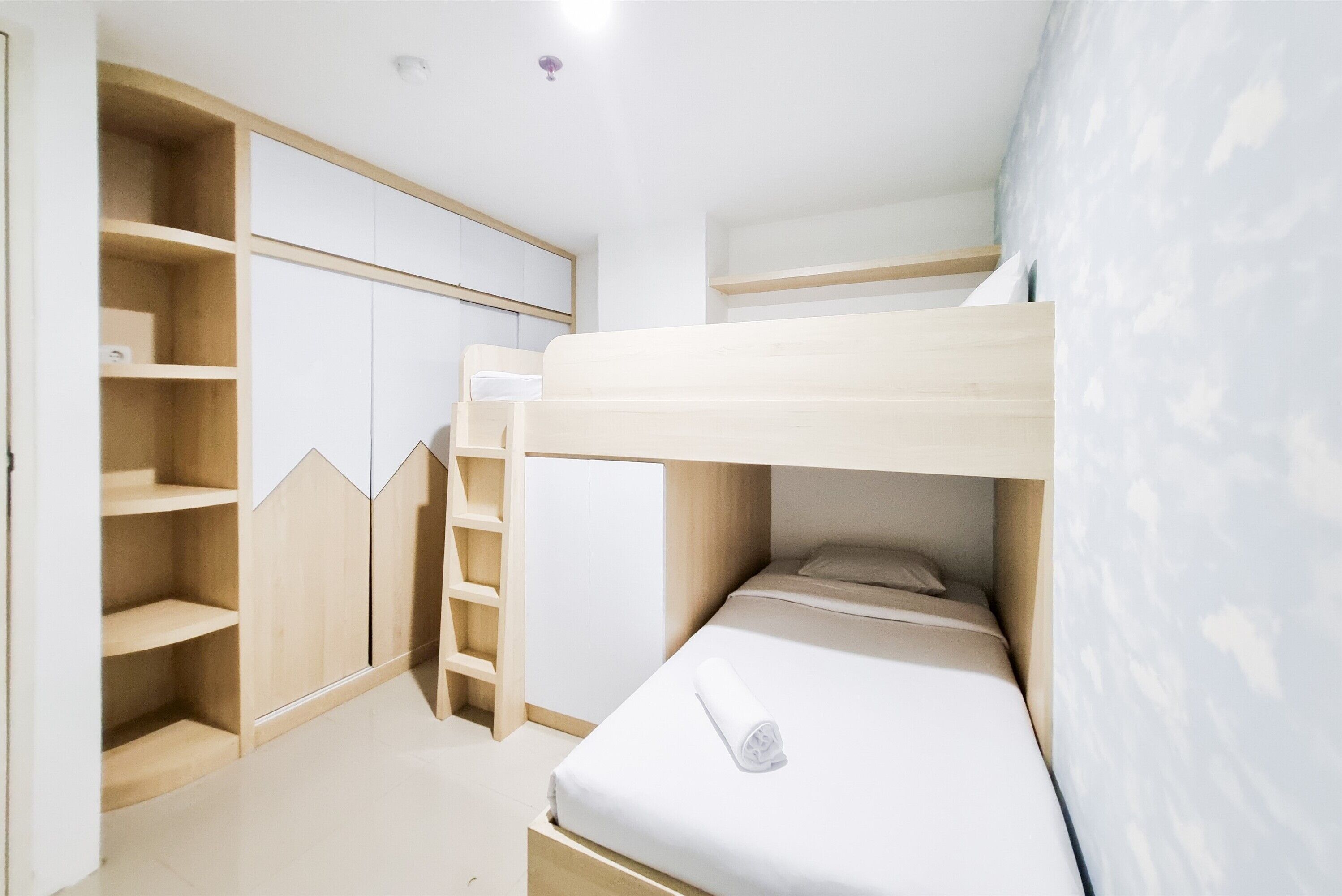 Habitación con literas, una escalera de madera, estantes integrados y un colchón blanco.