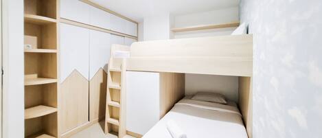 Habitación con literas, una escalera de madera, estantes integrados y un colchón blanco.