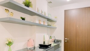 A kitchen with grey countertops, a wooden door, and shelves with plants and kitchenware. - Relaxing Studio At Transpark Cibubur Apartment (Depok)