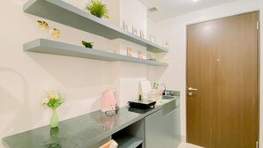A modern kitchen with grey countertops, a wooden door, and built-in shelves with plants and kitchen items. - Relaxing Studio At Transpark Cibubur Apartment (Depok)