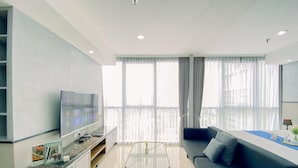 A modern living room with a flat-screen TV, a sofa, a coffee table, and a balcony with curtains. - Good Deal And Elegant Studio Ciputra World 2 Apartment (Jakarta)