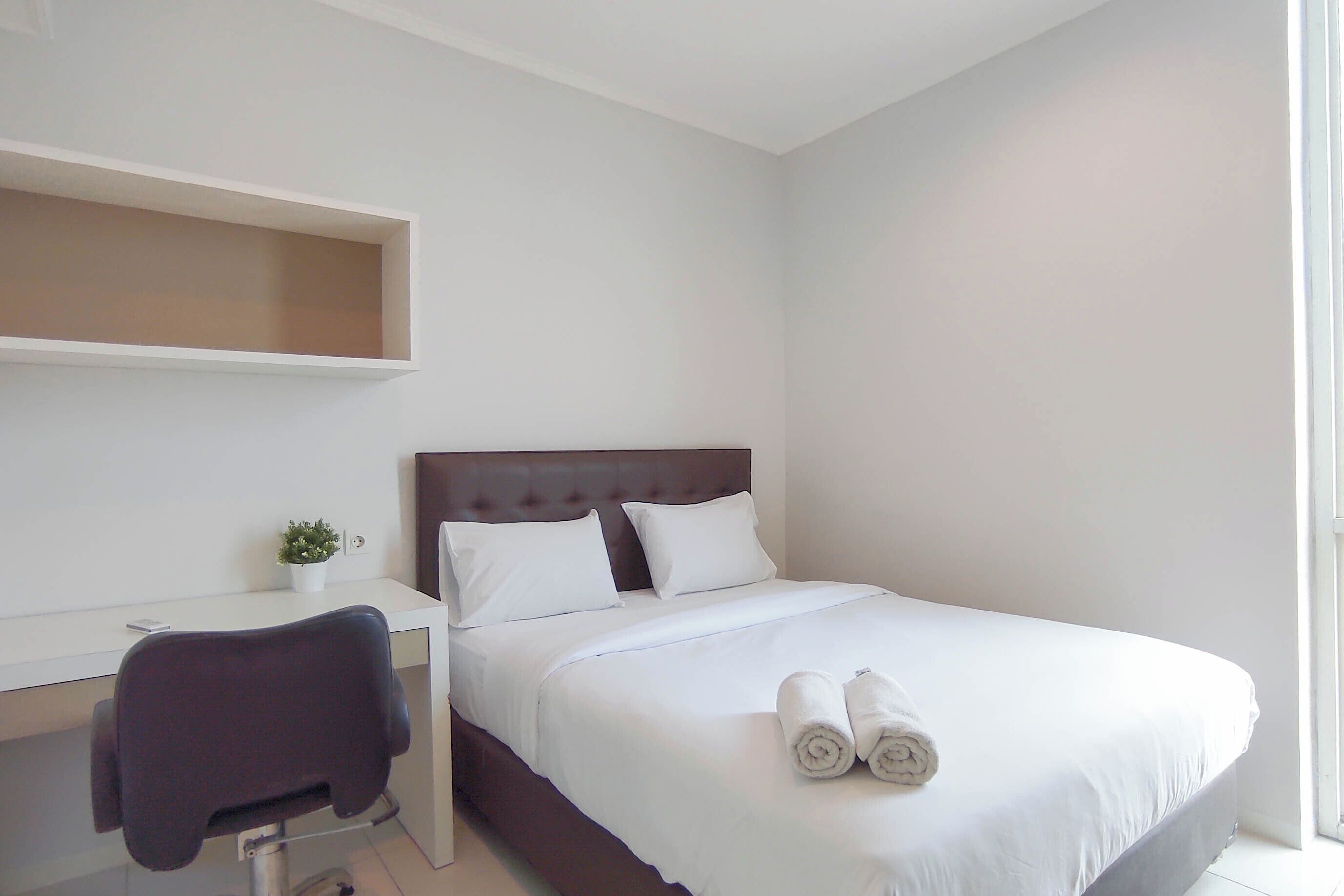 A neatly arranged hotel room with a bed, a desk, and a chair.