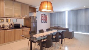 Una cocina moderna con armarios de madera, un refrigerador de acero inoxidable y un comedor con mesa y sillas de vidrio.