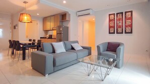 Una sala de estar moderna con un sofá gris, una mesa de centro de vidrio y una zona de comedor con mesa y sillas.