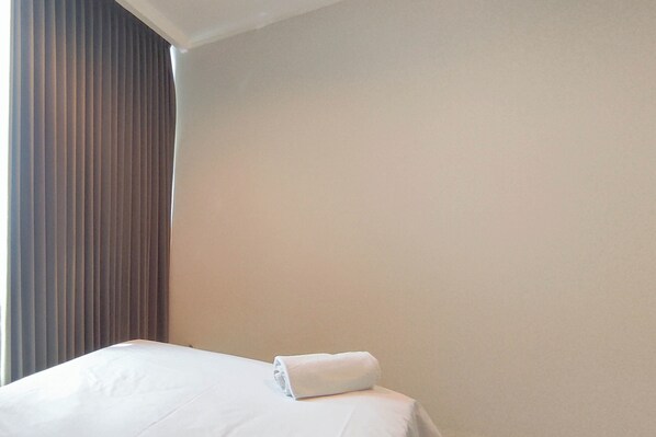 Un lit bien fait, avec une serviette blanche roulée posée sur la tête de lit, dans une chambre d’hôtel.