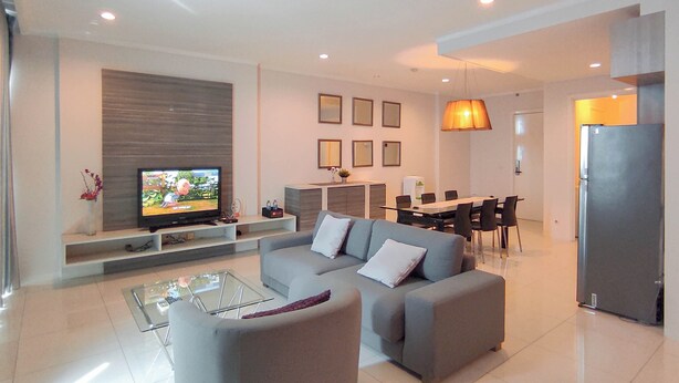 Una sala de estar moderna con un televisor de pantalla plana, un sofá gris, una mesa de centro de vidrio y un comedor con mesa y sillas.