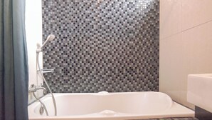 Un baño con pared de mosaicos, una bañera blanca y un cabezal de ducha.