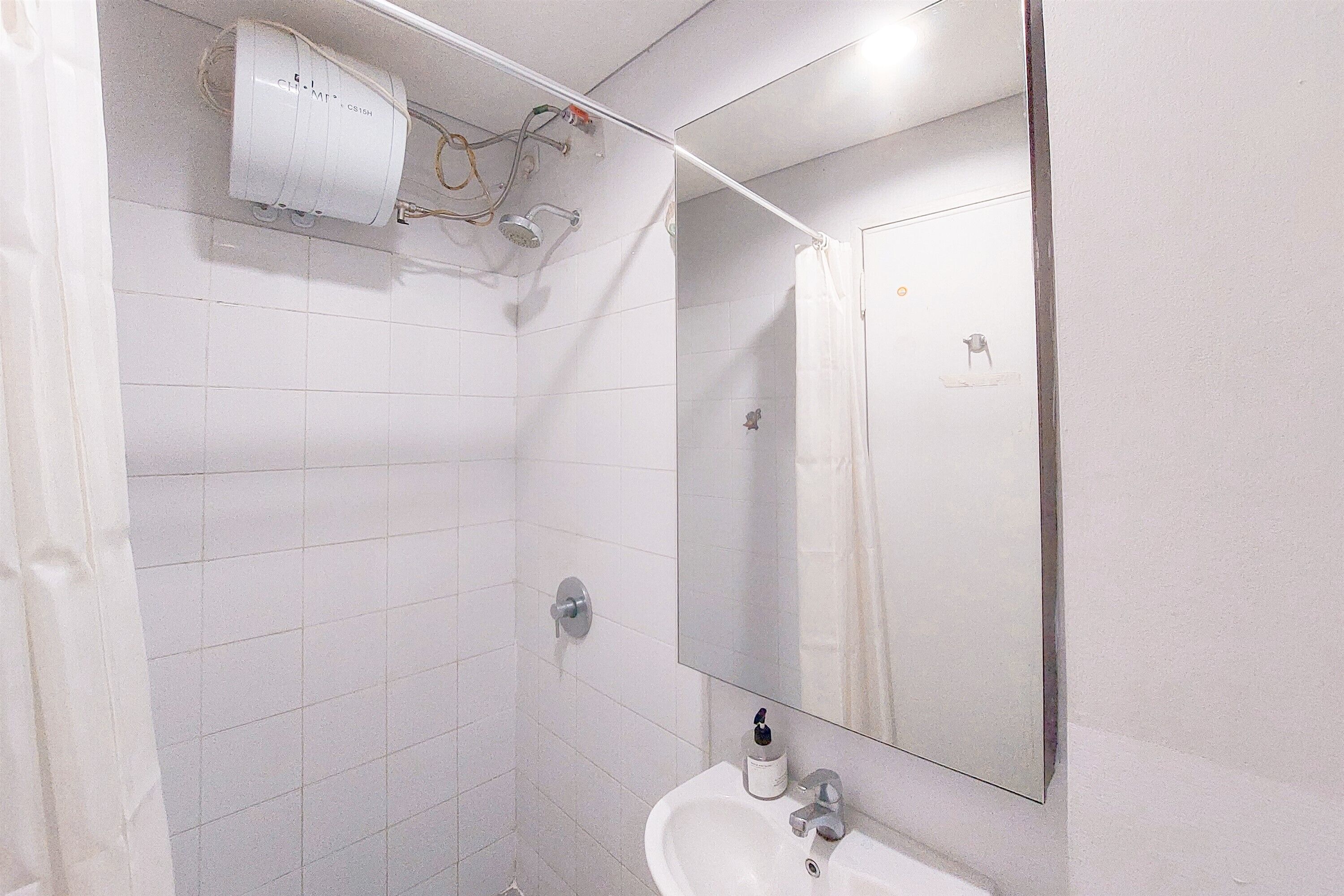 A bathroom with white tiles, a sink, a mirror, and a shower.