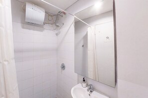Een badkamer met witte tegels, een wastafel, een spiegel en een douche.