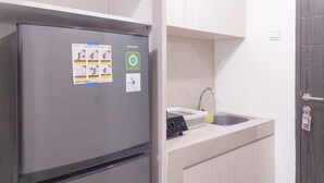 A compact kitchen with a stainless steel refrigerator, a built-in sink, and light-colored cabinetry. - Restful And Tidy Studio At Apartment Baileys (South Tangerang)