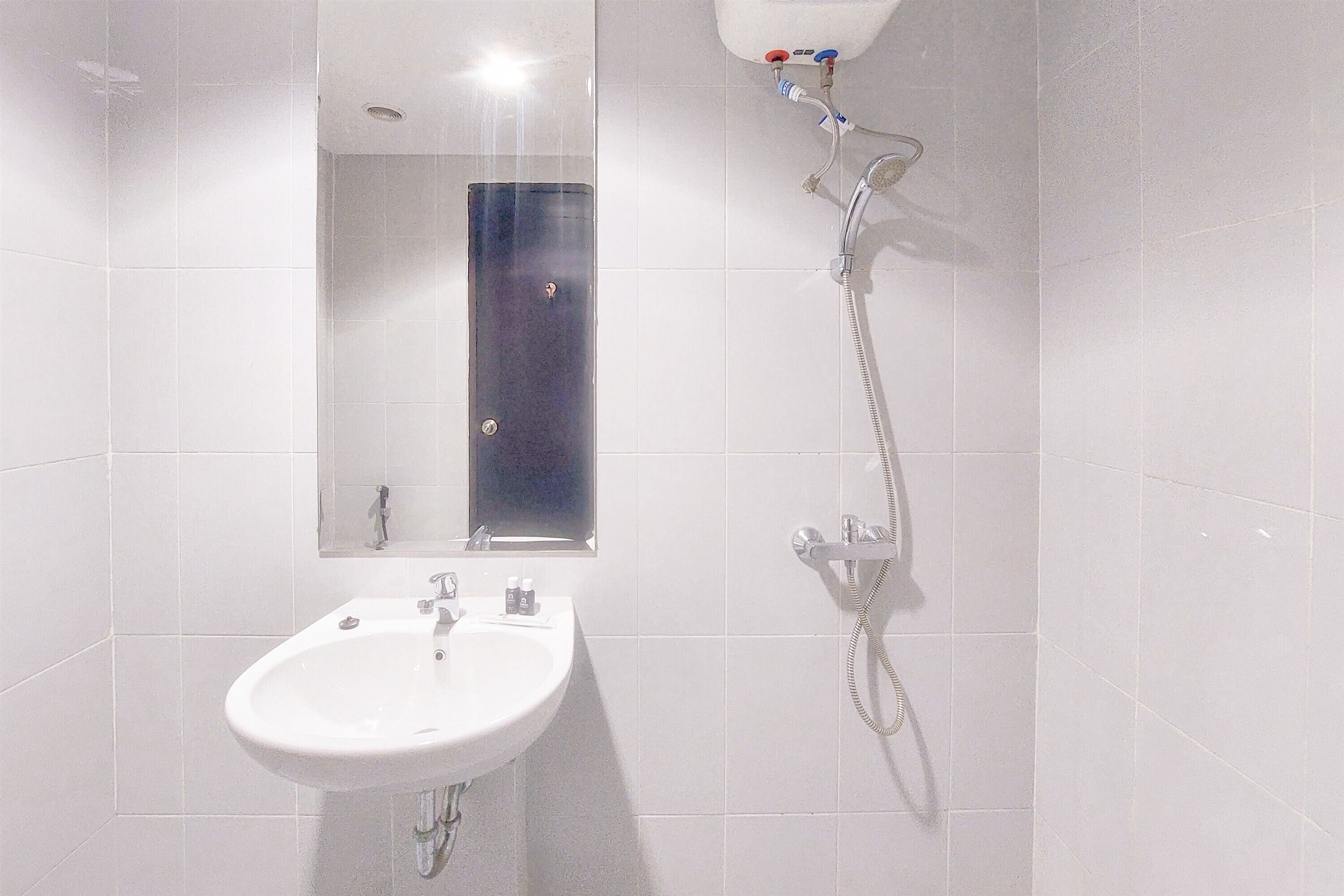 Casa de banho com lavatório branco, espelho e chuveiro com chuveiro manual.