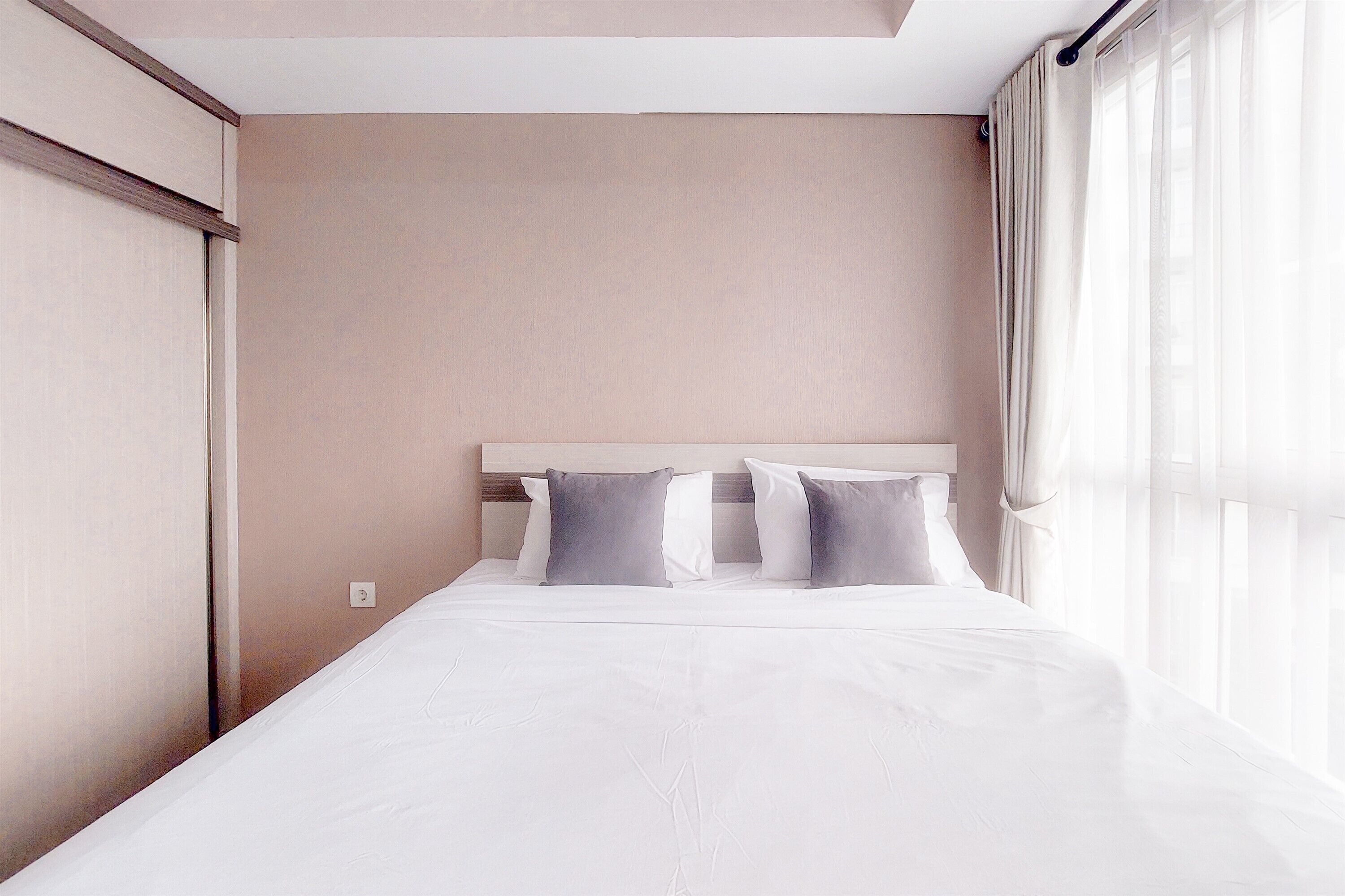 A neatly made bed with a headboard, a window with curtains, and a wall with a light switch.