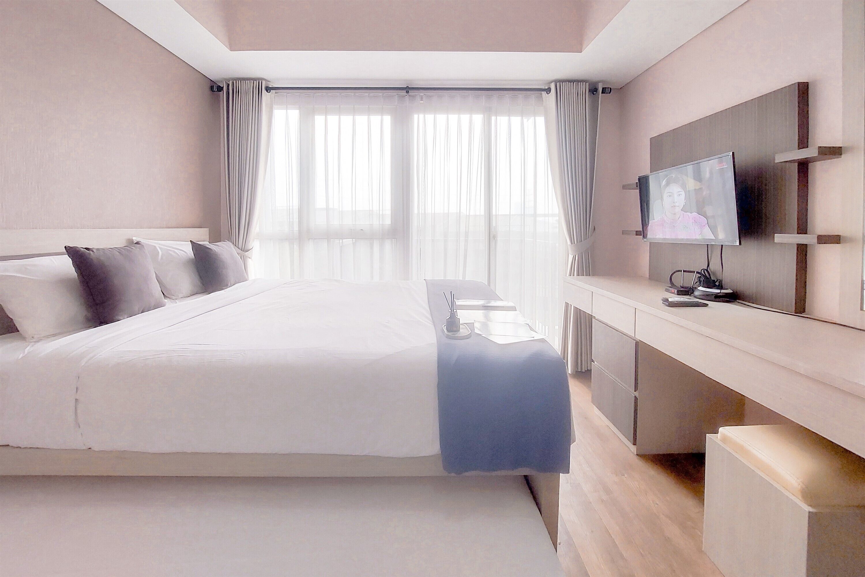 A modern hotel room with a large bed, a bedside table, a TV, and a desk area.