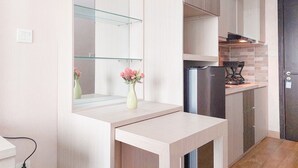 A modern kitchen with a built-in stove, a refrigerator, and a glass shelf unit. - Comfy And Homey Studio At Casa De Parco Apartment (Pagedangan)