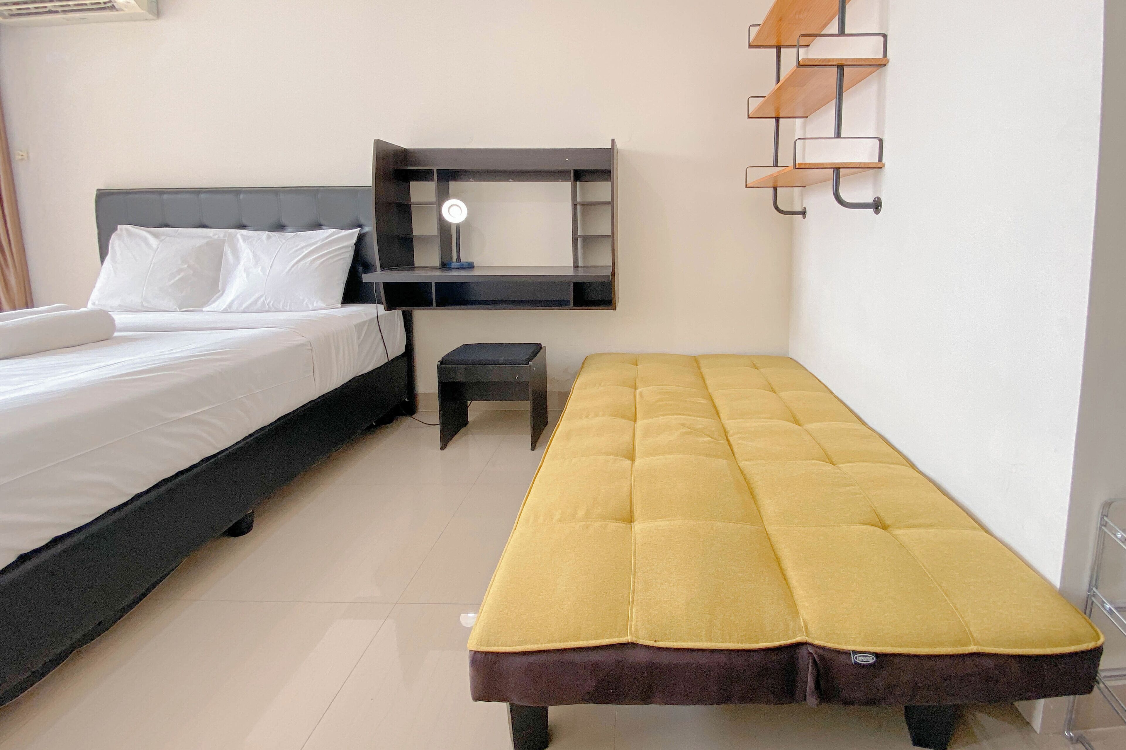 Un dormitorio con cama, un banco, un escritorio con lámpara y una estantería.