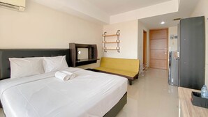 A hotel room with a large bed, a TV, a small sofa, a wooden door, and a refrigerator. - Highrise Studio At Apartment Beverly Dago (Bandung)