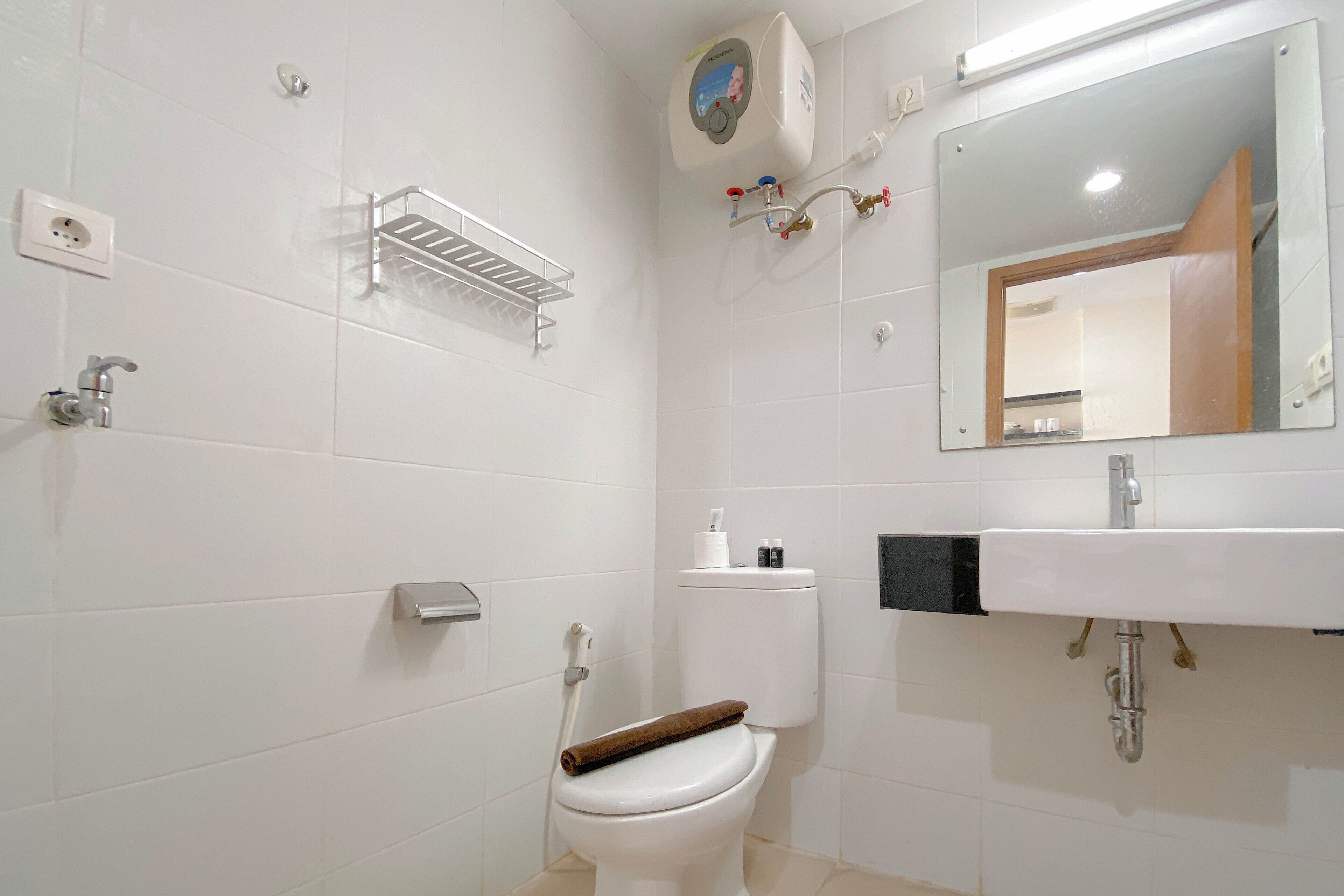 A bathroom with a toilet, a sink, a mirror, and a showerhead.